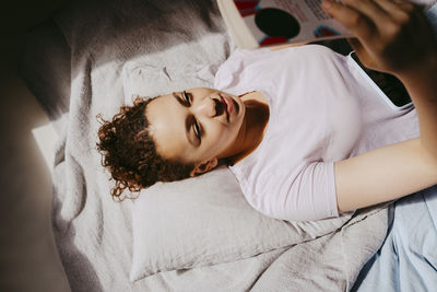 High angle view of teenage girl reading book while lying on bed at home