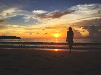 Silhouette woman standing on beach against sky during sunset