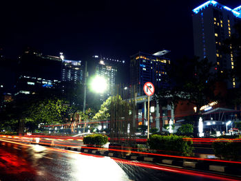 Light trails on road along illuminated buildings at night