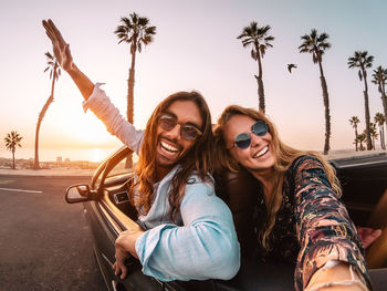 Portrait of cheerful couple wearing sunglasses in convertible against sky