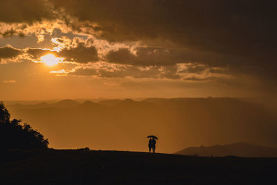 Silhouette people standing on mountain against sky during sunset