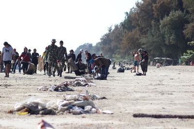 People cleaning garbage at beach against clear sky