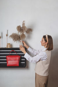 Woman millennial fashion stylist decorates a shelf with a red bag with a pampas grass vase