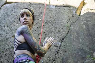 Tattooed girl rock climbing with friend on summer day