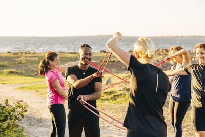 Smiling male and female teammates exercising together with resistance bands during group training session at beach