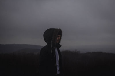 Young man wearing fur coat against cloudy sky during foggy weather