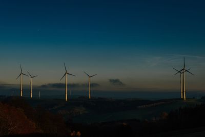 Wind turbines on field against sky during sunset