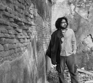 Thoughtful young man holding jacket while standing against brick wall