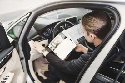 High angle view of man reading brochure while sitting in car at store