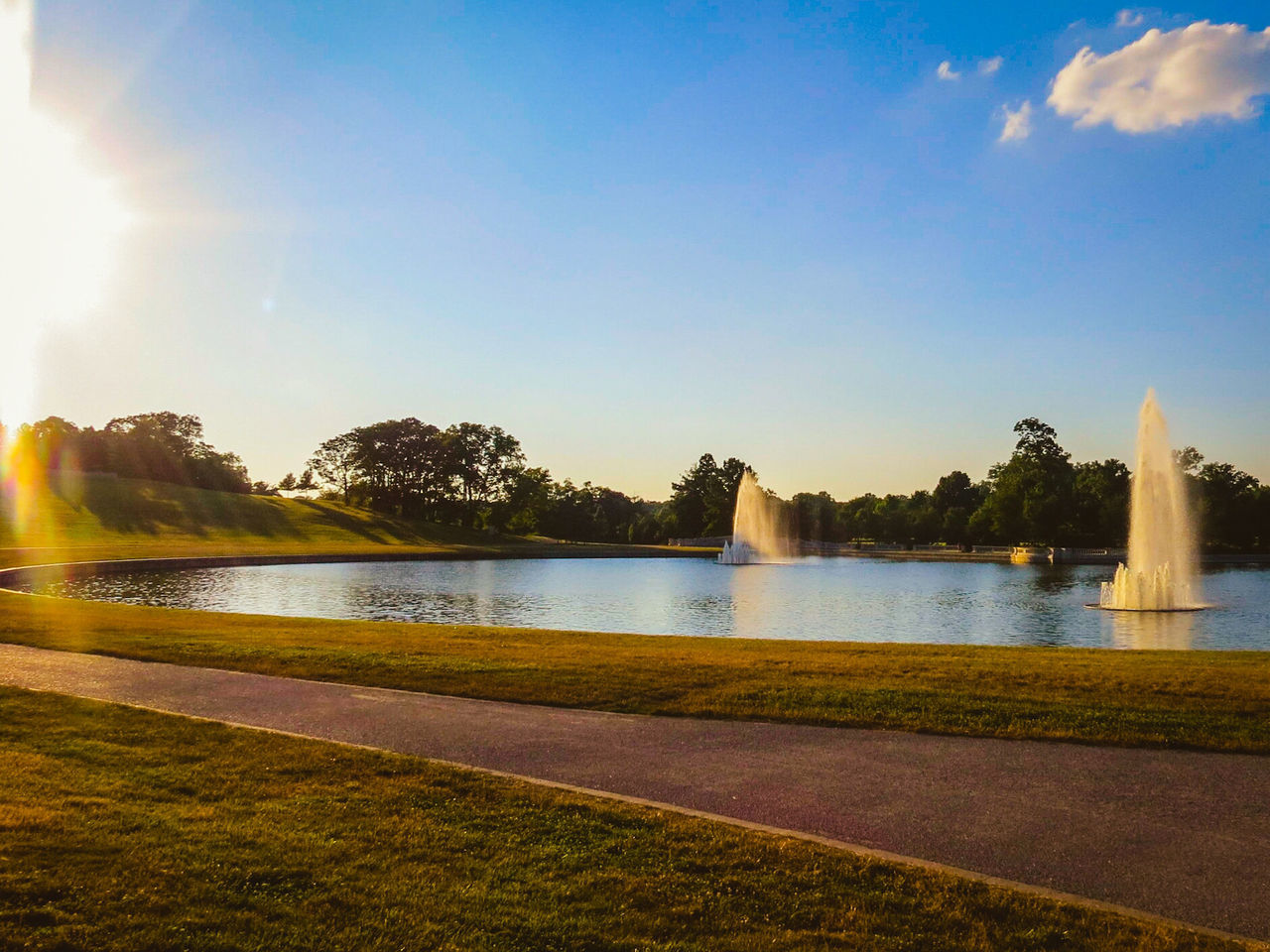 water, built structure, architecture, sunlight, sky, sunbeam, sun, river, bridge - man made structure, lens flare, tree, building exterior, blue, nature, railing, fountain, travel destinations, outdoors, connection, tranquility