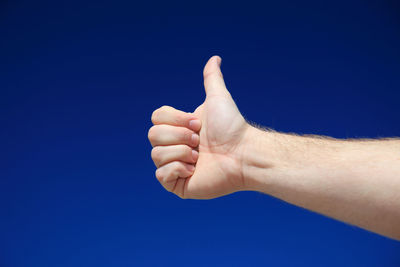 Cropped hand of man showing thumbs up against clear blue sky