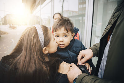 Sister kissing on brother's cheek while sitting on bicycle seat with father in city