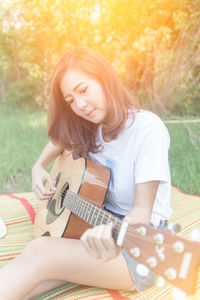 Young woman playing guitar on grassy field at park