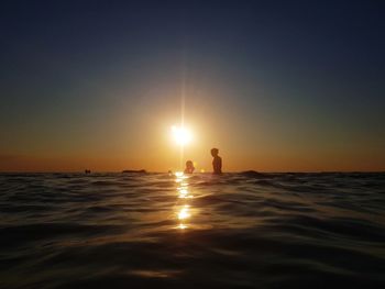 Silhouette people on sea against sky during sunset