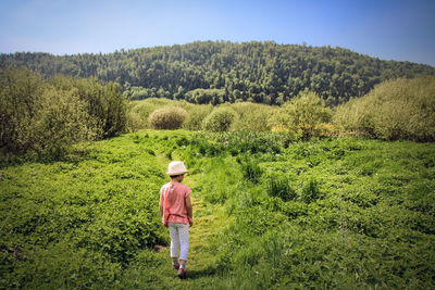 Rear view of girl walking on grassy field