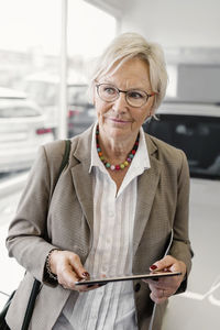 Senior businesswoman with digital tablet standing in car dealership store