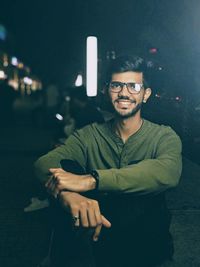 Smiling young man wearing eyeglasses while looking away at night