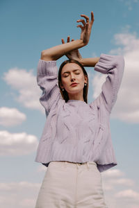 Young woman with arms raised standing against sky