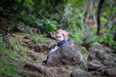 Portrait of girl sitting on rock in forest