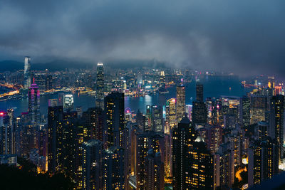 Illuminated buildings in cityscape against cloudy sky at night