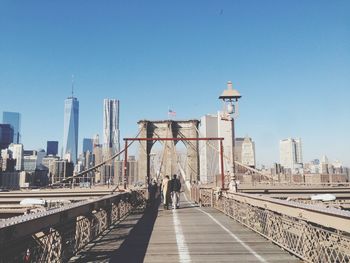 Rear view of people walking on brooklyn bridge by city against clear blue sky