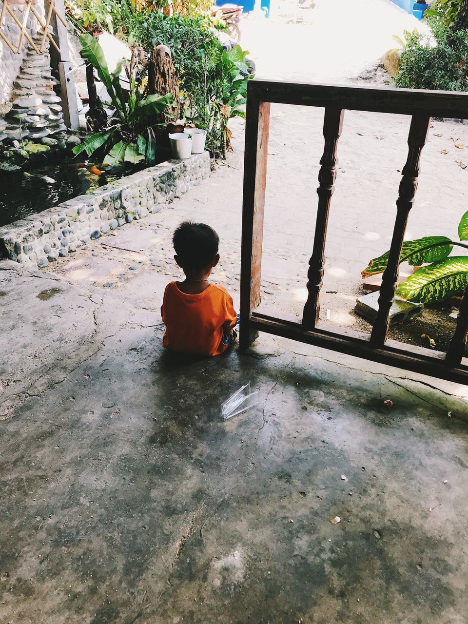 REAR VIEW OF BOY LOOKING AT MAN SITTING ON STONE WALL