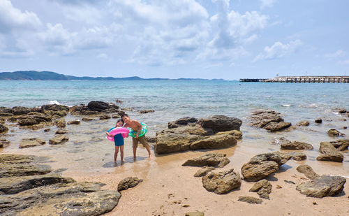 Siblings with inflatable rings standing on shore at beach