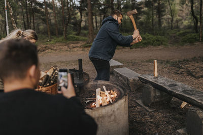 Man taking picture of friend chopping wood