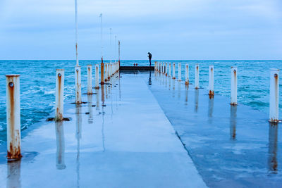 Lonely man standing on a sea pier and texting on smartphone, blue evening seascape