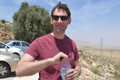 Portrait of young man holding water bottle on hill against sky