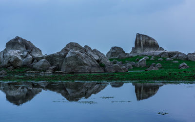 Reflection of rocks in lake against clear sky