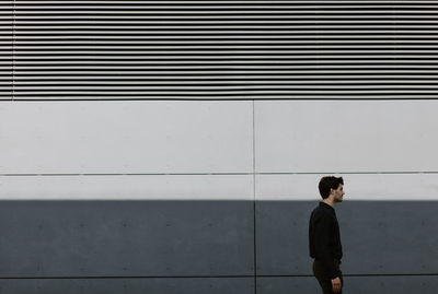 Young man looking away standing against wall
