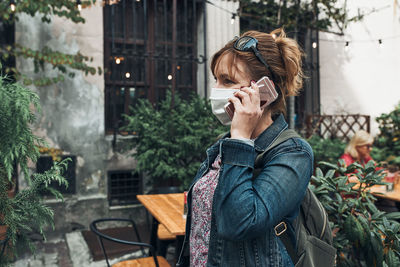 Young woman talking on phone standing in a street downtown. woman is wearing the face mask