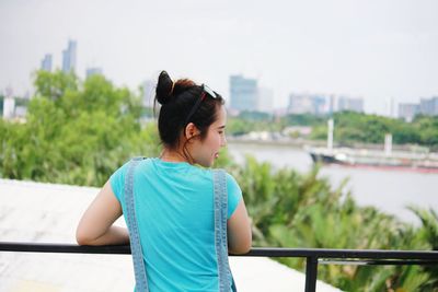 Young woman looking away while standing on railing in city