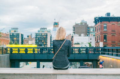 Rear view of woman sitting on steps against buildings in city