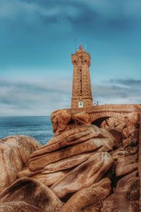 View of lighthouse on beach against cloudy sky