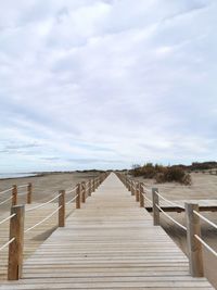 Wooden boardwalk on beach against sky