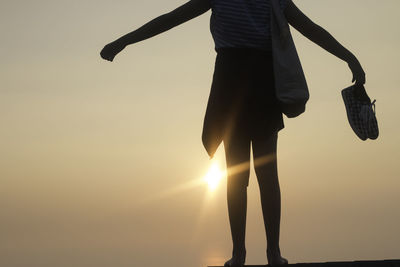 Low section of woman standing against sky during sunset