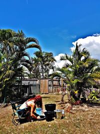 Woman sitting on palm tree against sky