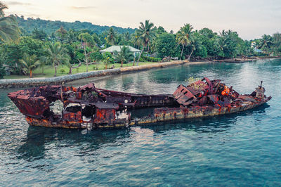 Broken rusty boat in water near tropical shore against of palm trees and forest. sanma, vanuatu.