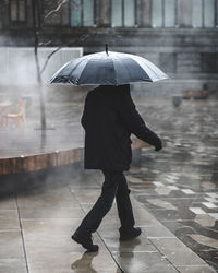 Rear view of man walking on wet street during monsoon
