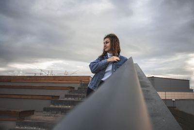 Surface level shot of woman looking away against cloudy sky