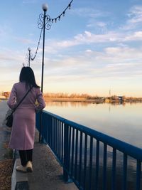 Rear view of woman standing by railing against sky