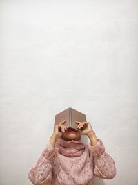 Midsection of woman holding book while standing against white wall