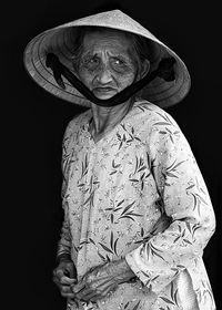 Close-up of senior woman wearing hat standing against black background