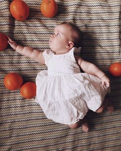 Baby girl wearing a princess dress laying on a mat trying to reach an orange 