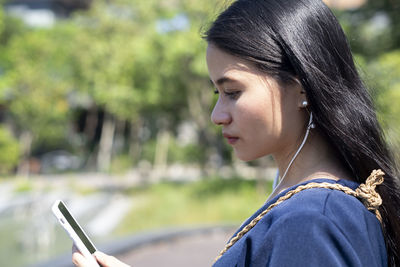 Close-up portrait of young woman using mobile phone outdoors