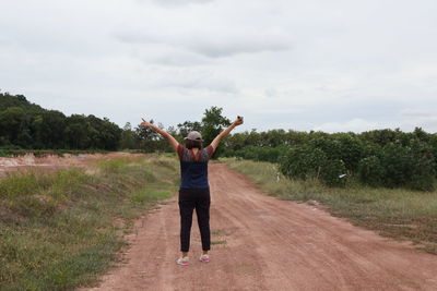 Rear view of woman standing on road amidst field against sky