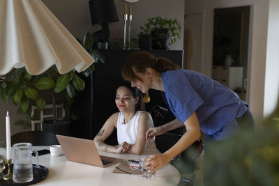 Female caregiver talking to woman with paraplegia watching laptop at home