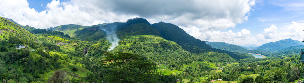 Panoramic landscape of sri lanka. waterfall in the mountains and tea plantation. smoke behind trees.